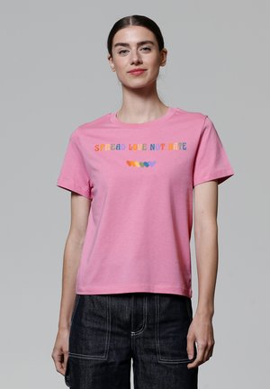 T-shirt en coton rose avec le texte "RÉPANDRE L'AMOUR PAS LA HAINE" en lettres multicolores et des cœurs coordonnés en dessous. Manches courtes et col rond.