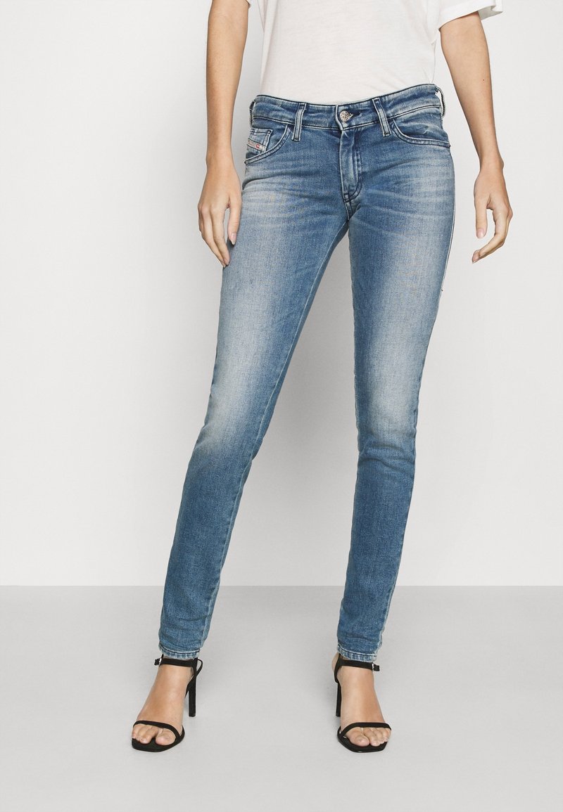 Kapeat siniset farkut, joissa on haalistunut pesu, etutaskut ja nappisulku, yhdistettynä mustiin hihnakenkiin.