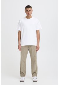 Hvid bomuldst-shirt med rund halsudskæring og korte ærmer, kombineret med beige bredbenede bukser i fløjl og hvide sneakers.