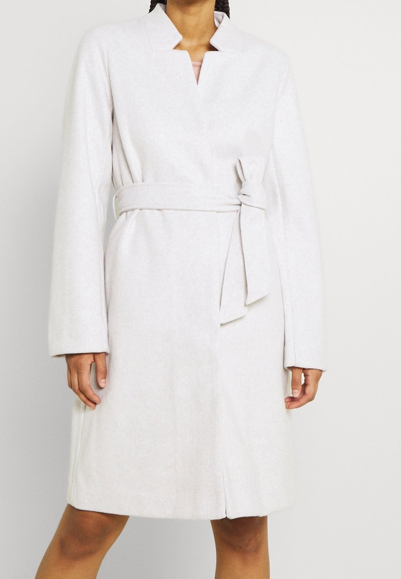 Jasnoszary płaszcz z paskiem, z kołnierzem typu szal, długimi rękawami i miękką, teksturowaną tkaniną. Posiada fason kopertowy oraz boczne rozcięcia.