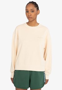 Cremfarbener Sweatshirt mit lockerer Passform, gerippten Bündchen und Saum sowie dezentem Logodetail. Kombiniert mit grünen Shorts mit seitlichen Akzenten.