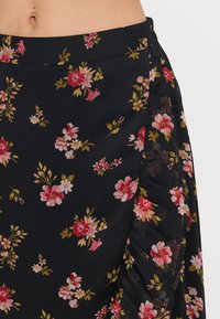 Svartblomstret skjørt med en blanding av rosa og gullblomster, med plisse-detaljer på siden og et glatt, lett stoff.