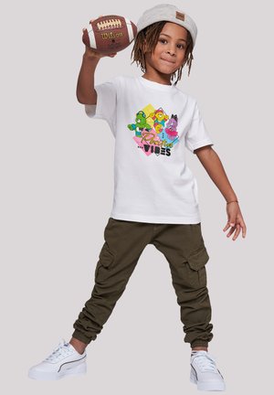 White t-shirt features colorful cartoon designs with "Positive Vibes" text. Olive green cargo pants and white sneakers with textured soles.