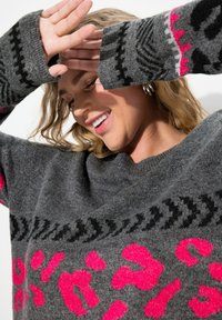 Maglione grigio realizzato in materiale morbido con una stampa leopardata rosa audace. Accenti neri a motivo su maniche e colletto. Vestibilità ampia e rilassata.