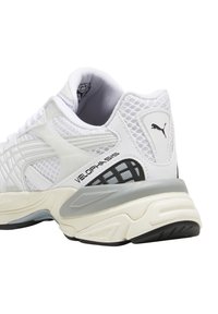 Weiße Sport schuh aus Mesh und synthetischen Materialien, mit einer strukturierten Ferse, Markenlogo an der Seite und grauen Akzenten auf der Sohle.