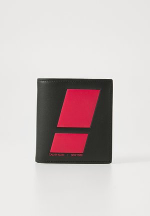 Zwarte leren portemonnee met een gedurfde rode geometrische print aan de voorkant. Tekst "CALVIN KLEIN / NEW YORK" in het rood onder het ontwerp.