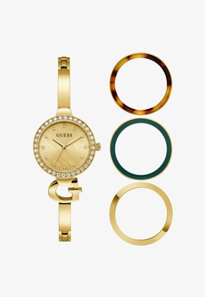 Zlaté hodinky Guess s lunetou zdobenou kryštálmi, vedľa tri vymeniteľné lunety v korytnačej, tmavozelenej a zlatej farbe.