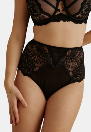 Sous-vêtements taille haute en dentelle noire et soutien-gorge assorti avec des panneaux en dentelle florale transparente portés par un mannequin féminin sur fond blanc.