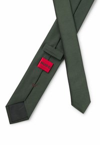 Grüne strukturierte Krawatte aus Stoff mit schmalem Design. Verfügt über ein rotes Etikett mit dem Text "HUGO". Schwarze Unterseite.