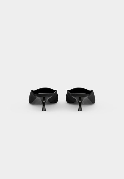 Ζευγάρι μαύρα μυτερά kitten heels με χαμηλά λεπτά τακούνια, απεικονισμένα από πίσω σε απλό ανοιχτό φόντο.