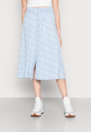 Jupe florale bleu clair, longueur genou, avec des motifs blancs, dotée d'une fente devant et d'une fermeture à boutons. Assortie à des baskets blanches à semelles épaisses.