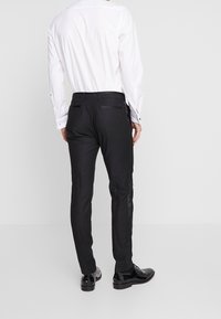 Svarta skräddarsydda byxor med sidofickor och bakfickor med knapp, tillsammans med en vit långärmad skjorta. Slät tygfinish.