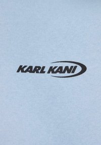 Gaiši zilā audumā ir melns "KARL KANI" logo ar izliekto apakšsvītru, kas izceļ gludu tekstūru un vienmērīgu audumu.