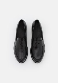 Mocassins en cuir noir à finition lisse, avec une couture autour de la semelle et une bande décorative sur le dessus. Semelle en caoutchouc antidérapante.