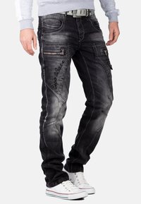 Zwarte denim jeans met een vervaagde afwerking, voorzien van ritszakken, gestikte details en een slim fit. Gecombineerd met witte sneakers.