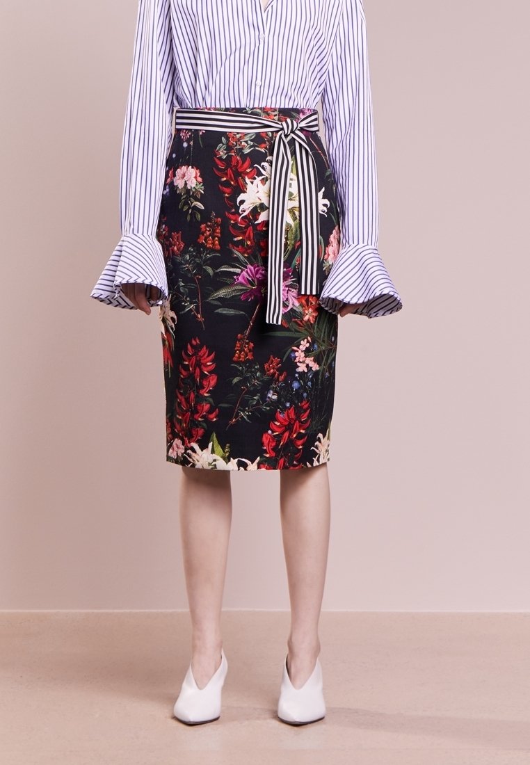 Jupe crayon florale avec fond sombre ; présente des fleurs tropicales colorées et des feuilles, ceinturée à la taille avec un tissu rayé.