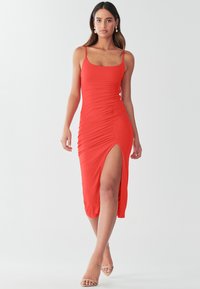 Czerwona sukienka dopasowana z cienkimi ramiączkami, marszczeniem po bokach i rozcięciem sięgającym uda. Wykonana z gładkiego, elastycznego materiału.
