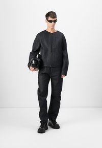 Dark denim jacket with a zip front, long sleeves, and pants in matching fabric. Black accessories include a handbag and chunky shoes.