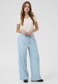 Pantaloni a gamba larga azzurro chiaro con vita regolabile, abbinati a una maglietta bianca attillata a scollatura a V. Texture liscia, design casual.