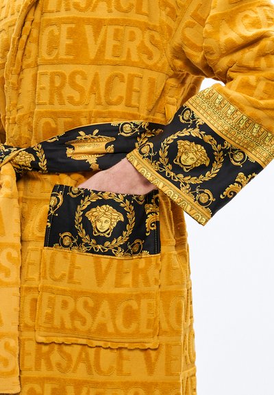 Zlata kopalna halja iz frotirja z vtisnjenim vzorcem "VERSACE", črni satenasti manšeti z zlatim motivom Meduze in okrašeni dekorativni poudarki.