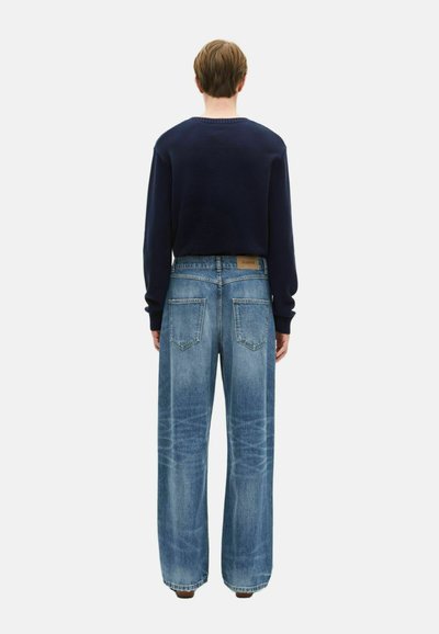 Maglione a girocollo blu marina abbinato a jeans a gamba larga in denim blu chiaro con un lavaggio sbiadito, cinque tasche e un'etichetta in pelle marrone sul retro.