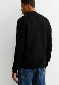 Czarny sweter dzianinowy o ryflowanej fakturze, okrągłym dekolcie i dopasowanych mankietach, w połączeniu z niebieskimi dżinsami z tylnymi kieszeniami.