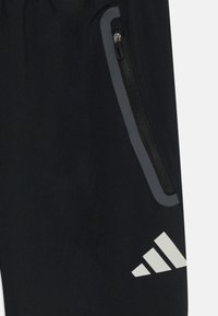 Črna tkanina z žepom na zadrgo, obrobljenim z odsevnim trakom, in belim logotipom s tremi črtami blizu spodnjega desnega kota.