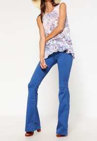 Jeans in denim blu con taglio a zampa, dalla texture liscia, abbinati a un top estivo leggero senza maniche, caratterizzato da un orlo arricciato e colori pastello delicati.