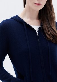 Felpa con zip navy realizzata in tessuto morbido, con zip frontale, cappuccio e maniche lunghe con lacci. Design semplice e minimale.