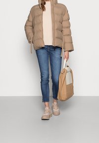 Beige dunjakke med lynlås og hætte, lys beige sweater, blå skinny jeans, beige sneakers og en tan tote bag med en lys accent.