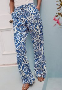 Valkoiset kangashousut, joissa sinisiä kukka- ja geometrisia kuvioita, väljät, kuminauhavyötärö, taskut ja suora lahjemalli.