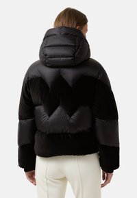 Sort dunjakke med polstret hætte, der har et zigzag-mønster over ryggen. Tekstureret stof, der kontrasterer med glatte sektioner.