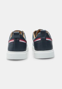 Marineblaue Ledersneaker mit einer weißen Gummisohle, die rote und weiße Akzentstreifen an der Rückseite und eine Schlaufe für einfaches Anziehen aufweisen.