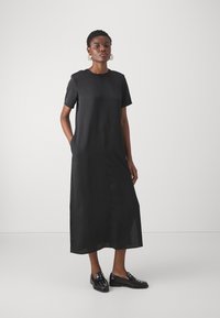 Rochie midi neagră cu mânecă scurtă, decolteu rotund, buzunare laterale și o siluetă dreaptă. Modelul poartă pantofi negri cu detalii decorative.
