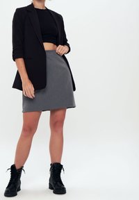 Blazer nero con le maniche arrotolate su un crop top nero aderente, abbinato a una gonna A-line grigia e stivali da combattimento neri con lacci.