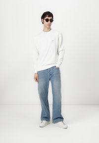 White sweatshirt with a logo on the chest, paired with light blue wide-leg jeans and white sneakers. Black sunglasses complete the look.