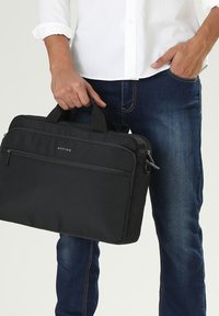 Zwarte laptoptas met dubbele bovenhandvatten, gemaakt van textuurstof. Bevat een voorklep met rits en logo-detail aan de voorkant.