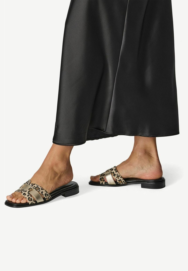 Sandales à enfiler à imprimé léopard avec des accents métalliques dorés et une semelle noire plate ; conçues avec des larges brides pour le confort et le style.