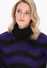 Maglione a righe viola e nere con collo alto a coste. Tessuto morbido, vestibilità ampia, con variazioni di colore in un motivo ondulato.