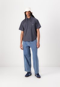 Karirana kratka srajca v mornarski in svetlo modri barvi z ovratnikom na gumbe, v kombinaciji s svetlo modrimi ravnimi jeans hlačami in mornarskimi supergami.
