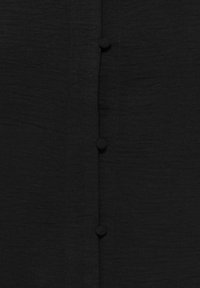 Gros plan sur un tissu noir avec trois boutons recouverts de tissu, espacés uniformément le long de la couture centrale.