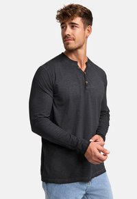 Schwarzes Langarm-Henley-Shirt aus strukturiertem Stoff, mit Knopfdetails am Ausschnitt und figurbetonten Ärmeln, kombiniert mit hellblauen Jeans.