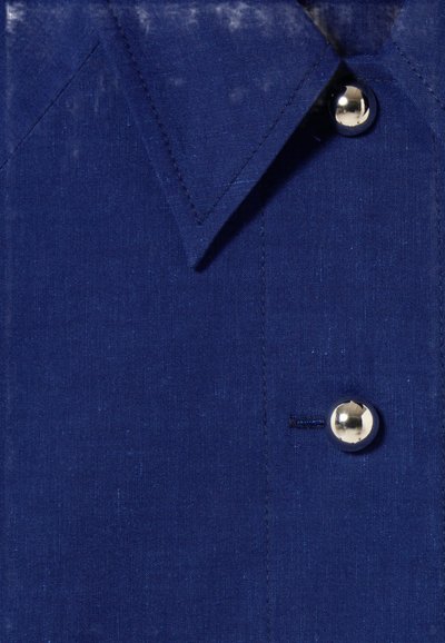 Chemise en lin bleu marine avec un col pointu, un bouton argenté et une poche poitrine. Le tissu a une texture et un brillant subtils.