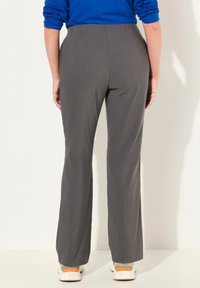 Pantalons gris évasés en tissu lisse, avec une taille élastique, portés avec des baskets blanches aux accents orange.
