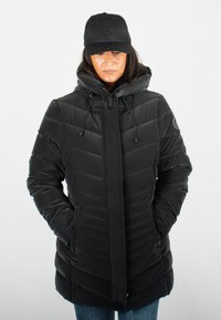 Doudoune noire avec capuche, présentant un design matelassé vertical, des poches latérales et des cordons réglables. Associée à une casquette noire.