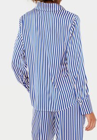 Blå och vitrandig långärmad skjorta med krage, med knappslå på ärmslut och avslappnad passform. Tyget verkar mjukt och lätt.