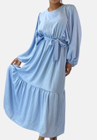 Lyseblå, langærmet maxikjole med et lagdelt design, indsnøret talje og stofbælte. Blød tekstur og flydende silhuet.