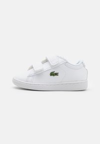 Zapatillas blancas para niños con dos correas de velcro, material sintético liso, punta redonda y un pequeño logo de cocodrilo verde en el costado.