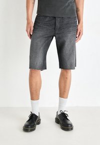 Shorts de mezclilla gris oscuro con un dobladillo deshilachado, que presentan un diseño clásico de cinco bolsillos. Combinados con zapatos negros y calcetines blancos acanalados.