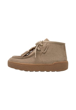 Beige suede ankle shoe with lace-up closure, decorative tassels and beads, and a thick textured rubber sole.
